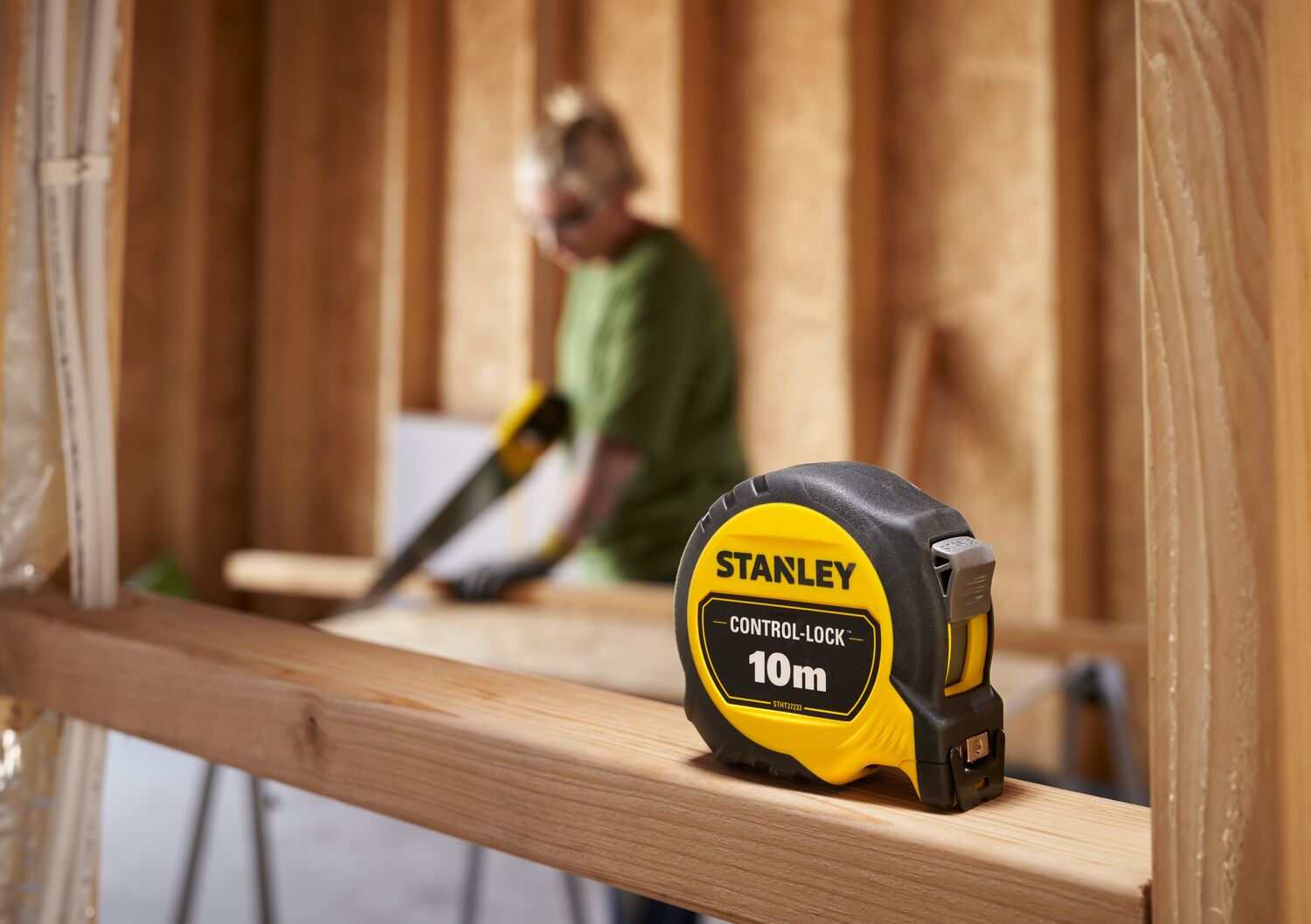 STANLEY® CONTROL-LOCK™ 10M (25mm wide) Tape Measure sitting on timber frame,  worker on site in background.
