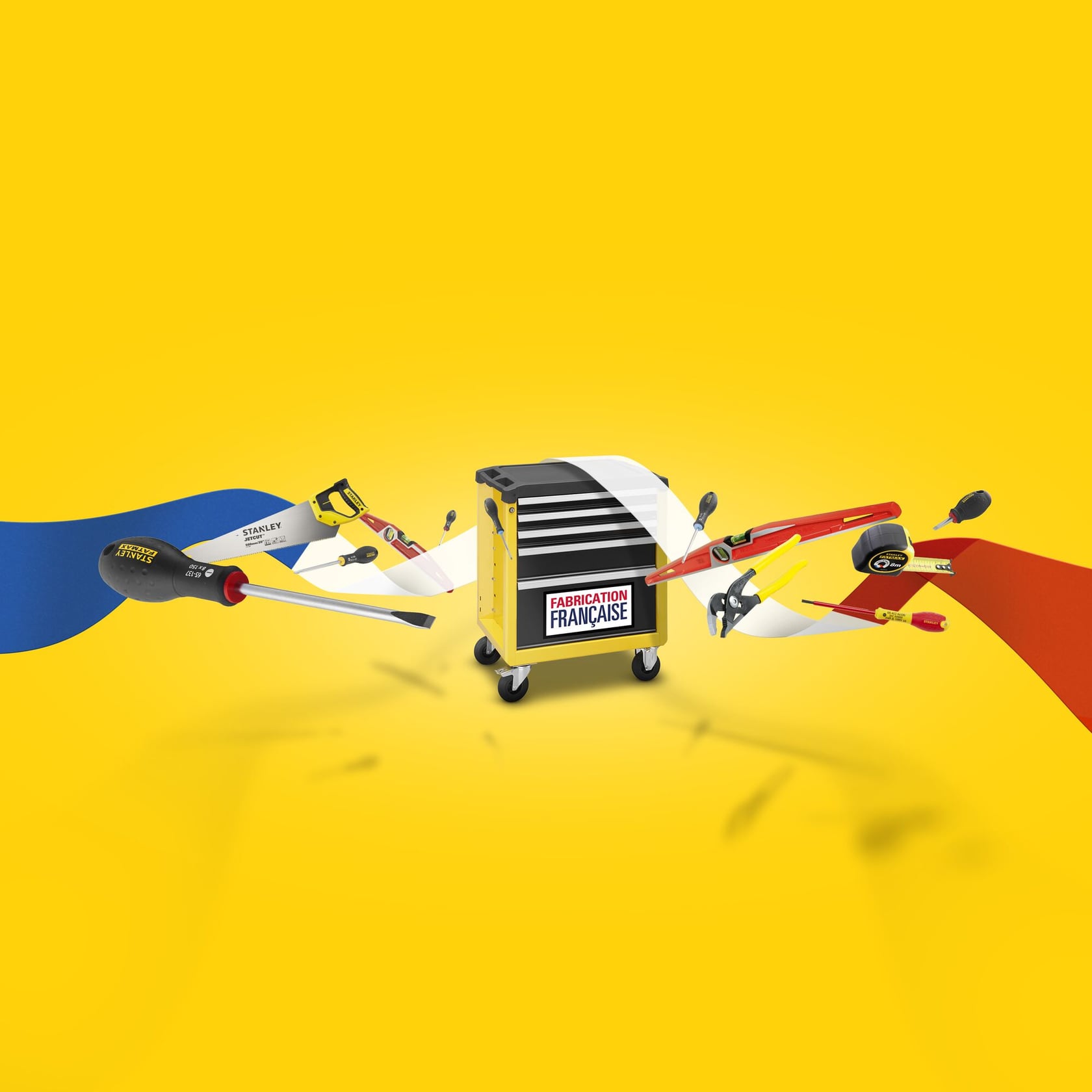A yellow Stanley tool chest on wheels with a 'Fabrication Française' (French manufacturing) label, surrounded by various hand tools such as screwdrivers, a saw, a tape measure, and a level, set against a bright yellow background with red, white, and blue ribbon-like shapes.
