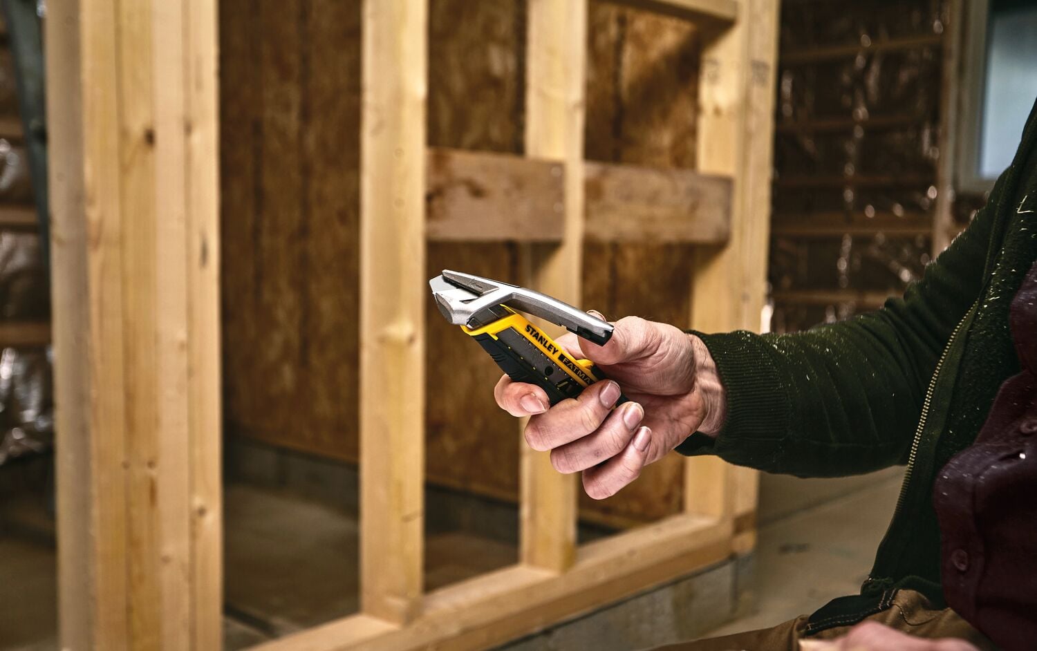 Couteau utilitaire STANLEY FMHT10592-0 tenu en main sur un chantier, poignée jaune et noire visible.